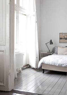 a bed sitting in a bedroom next to a window with white walls and wooden floors