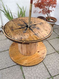 a wooden table with a clock on it sitting in the middle of a patio next to potted plants