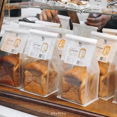 breads and pastries in plastic bags are on display at a bakery counter with people working behind them