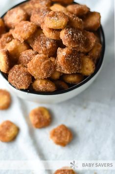 a bowl filled with sugar coated doughnuts on top of a white table cloth