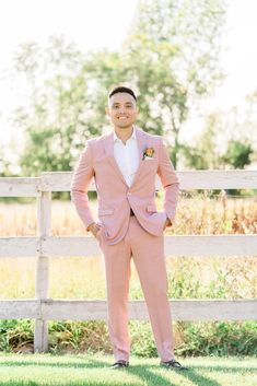 a man in a pink suit standing next to a wooden fence and grass area with his hands on his hips