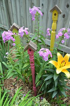 some purple and yellow flowers are in the grass next to a wooden fence with bird houses on it