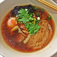 a white bowl filled with noodles and vegetables next to chopsticks on a table