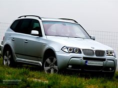 a silver car parked in the grass near a fence