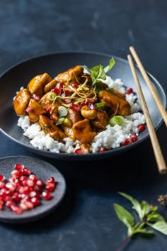 chicken and pomegranate on rice with chopsticks next to it in a black plate