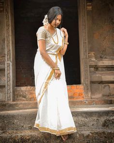 a woman in a white and gold sari standing on steps with her hand on her hip