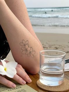 a woman's foot with a flower tattoo next to a glass of water on the beach