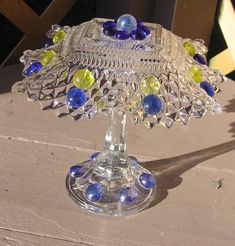 This unique glass mushroom is made from recycled glass, making it a very special piece! I just love repurposing old items that I find at various locations from stores to garage sales. I have found that glass is a material that continues to fascinate me with its inherent beauty and charm. The more items I make from glass, the more I get hooked on it! This glass mushroom is made using an outdoor glass glue with special blue and yellow glass globs to decorate it, on a clear cut-glass top and a clea Glass Globes Crafts, Glassware Garden Art, Blue Wine Bottles, Creative Garden Decor, Globe Crafts, Garden Fence Art, Garden Totem, Unique Garden Art, Glass Glue