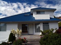 a white house with blue roof and bushes