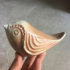 a hand holding a small ceramic bird on top of a tile floor next to a wall