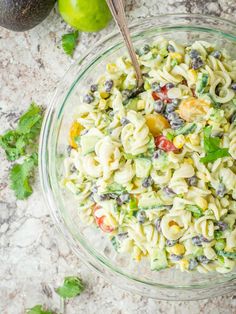 a glass bowl filled with pasta salad next to an avocado on the side