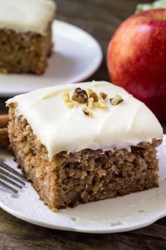 a piece of carrot cake with white frosting on a plate next to an apple