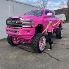 a woman standing next to a pink truck with big wheels on it's tires