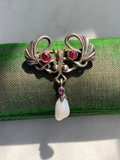 Marked: 800 (800 Silver), MO or OM? (maker's mark) Height: 1.20 inches Length: 0.98 inches Weight: 4.15 grams Features a pearl, red stones have not been tested Looks like a stylized Ginkgo Leaf, floral details, suspending a pearl Condition: Some light wear. Some extra glue on the pearl. Antique Jeweled Brooches For Gifts, Antique Jeweled Brooches For Formal Occasions, Red Brooch Jewelry For Formal Occasions, Antique Jeweled Brooches As Gift, Victorian Jeweled Brooches As Gift, Ornate Jeweled Brooches For Gifts, Art Nouveau Cabochon Brooches For Weddings, Ornate Jeweled Brooches As Gifts, Formal Ruby Brooch Jewelry