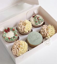 six cupcakes in a white box with frosting and holly wreath decorations on top