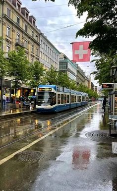 a blue and white train traveling down tracks next to tall buildings on a rainy day