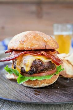 a bacon cheeseburger with lettuce and tomato on a plate next to a glass of beer