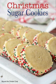 christmas sugar cookies with sprinkles are on a white plate next to candy canes