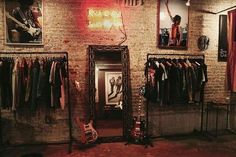 a room with clothes and guitars hanging on the wall, in front of a brick wall