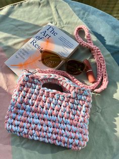 a pink and blue purse sitting on top of a bed next to a pair of sunglasses