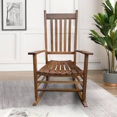 a wooden rocking chair sitting on top of a rug next to a potted plant