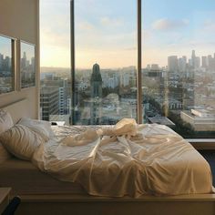 an unmade bed in front of a large window overlooking a cityscape and skyscrapers