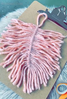 a pair of scissors and some yarn on top of a piece of paper with pink tassels