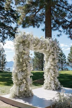 an outdoor ceremony with white flowers and greenery in the shape of a flower arch