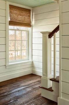 an empty room with wooden floors and white walls, along with a window in the corner