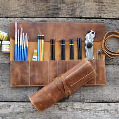 a leather case with pens, pencils, scissors and other items in it sitting on a wooden table