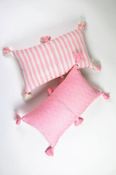 two pink and white pillows with tassels on the ends, one in striped fabric