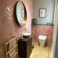 a bathroom with pink tiles and gold fixtures, including a round mirror above the sink