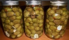 three jars filled with green olives sitting on top of a wooden table