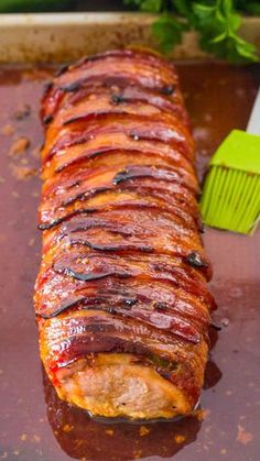 bacon wrapped pork tenderloin on a baking sheet with bbq sauce in the background