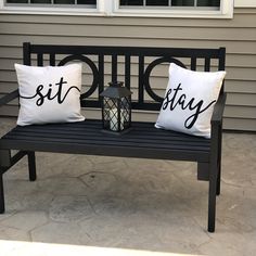 two pillows that say sit and stay on a black bench outside with a lantern next to it