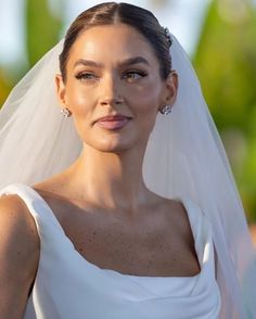 a woman wearing a white wedding dress and veil with diamond earrings on her head, looking at the camera