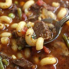 a spoon full of pasta soup with beef and green beans in the bowl is being held by a ladle