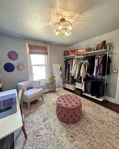 a room with a large rug, chair and shelves filled with clothes on hangers