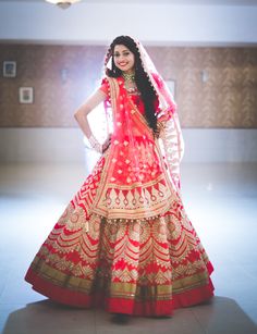 a woman in a red and gold bridal gown posing for the camera with her hands on her hips