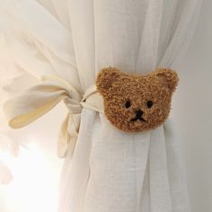 a brown teddy bear sticking out of the back of a white curtain with a bow