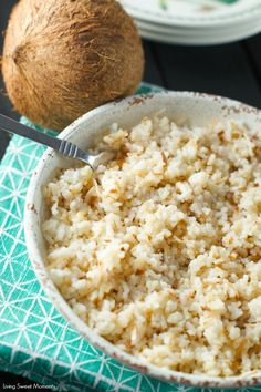 a bowl filled with rice next to a coconut on top of a green cloth and a fork