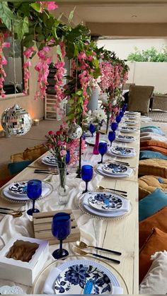 a long table is set with blue and white plates, silverware, and pink flowers