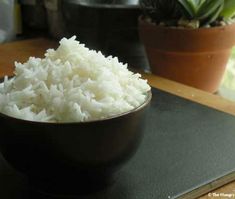 a bowl filled with white rice sitting on top of a table next to a potted plant