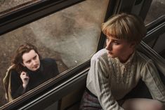 a woman sitting next to a man on a train looking at her reflection in the window