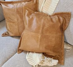 two brown leather pillows sitting on top of a couch next to a pillow and blanket