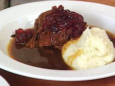 a white bowl filled with meat and mashed potatoes on top of a wooden table