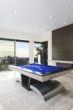 a pool table in the middle of a living room with large windows and city view