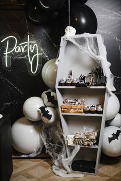 a halloween themed party with balloons, cake and other items on shelves in front of a black wall