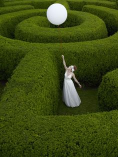 a woman in a pink dress is holding a white balloon while standing in the middle of a maze