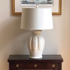 a white lamp sitting on top of a wooden table next to a painting and a framed picture